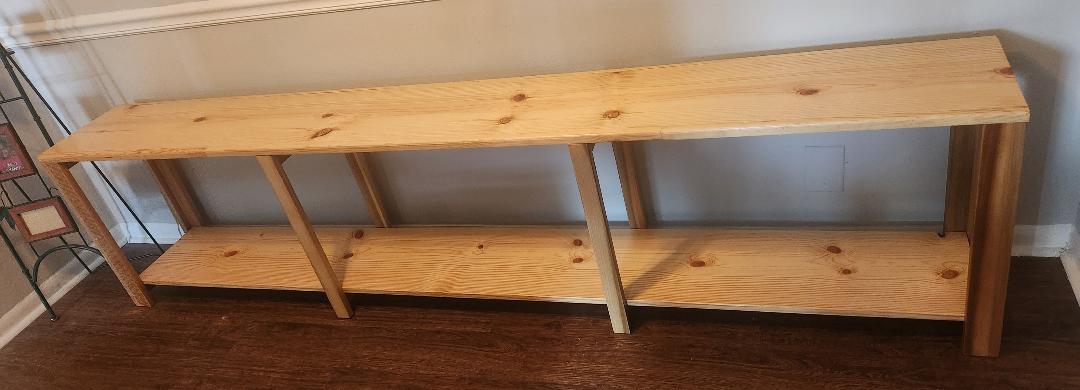 A long wooden storage shelf with pine shelves and poplar wood legs and cross braces.